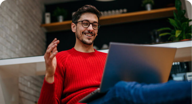 Smiling man with glasses and a red sweater using a laptop in a cozy home setting