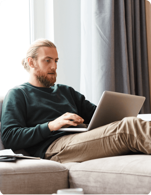 Bearded man with long blond hair sitting on a couch using a laptop