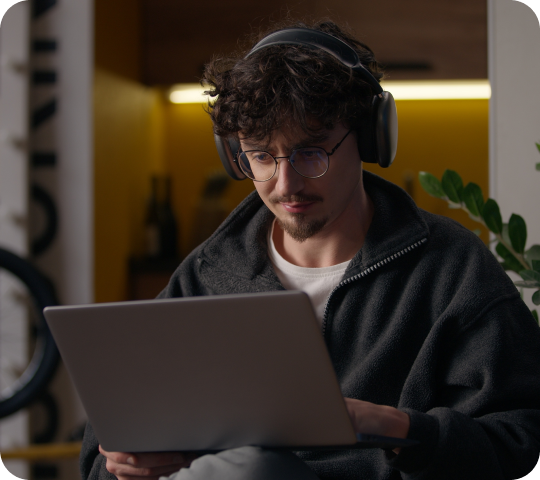 Person mit Kopfhörern arbeitet konzentriert am Laptop in gemütlichem Innenraum.