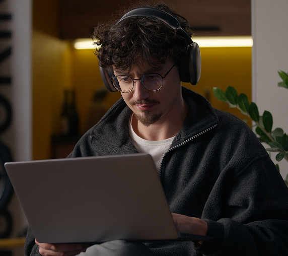 Person mit Kopfhörern arbeitet konzentriert an einem Laptop in einem gemütlichen Raum.